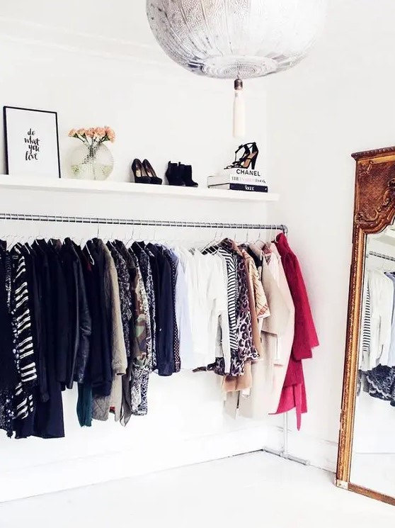 an elegant makeshift closet with a long railing for hanging clothes, an open shelf for shoes and other stuff and a mirror in a heavy frame