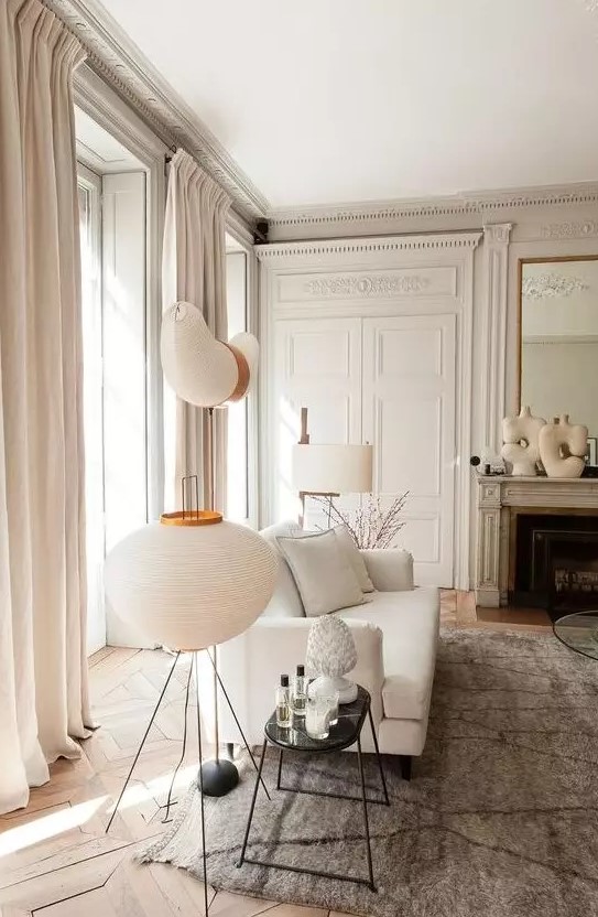 an elegant neutral French chic living room with off whites, greys and some beige touches is filled with light