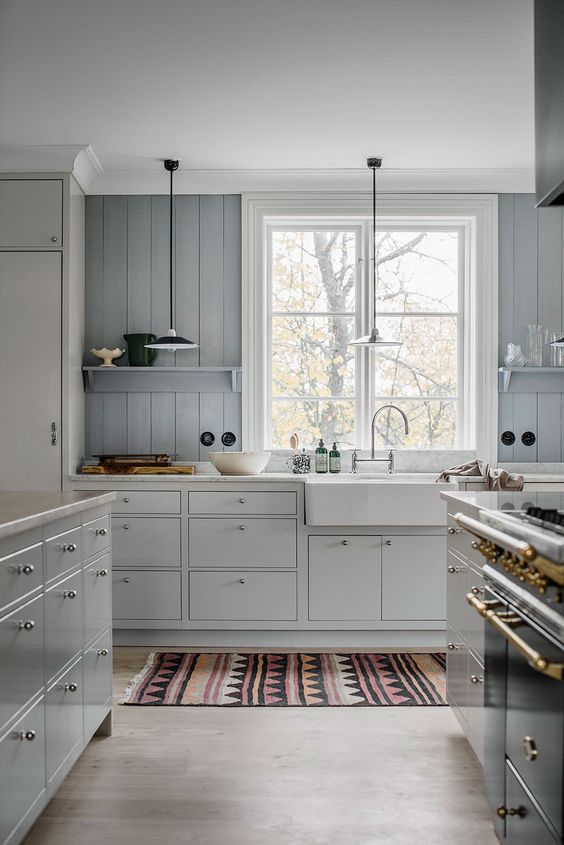 an ethereal kitchen with neutral cabinets, a ligth blue beadboard backsplash and a bold printed rug