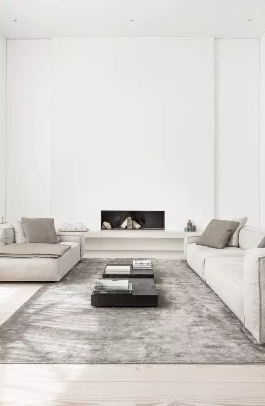 an ultra minimal living room in neutrals, with a built in fireplace, neutral furniture, black tables and a grey rug