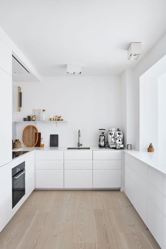 an ultra minimalist white kitchen with sleek cabinets, an open shelf, built in appliances and a large window