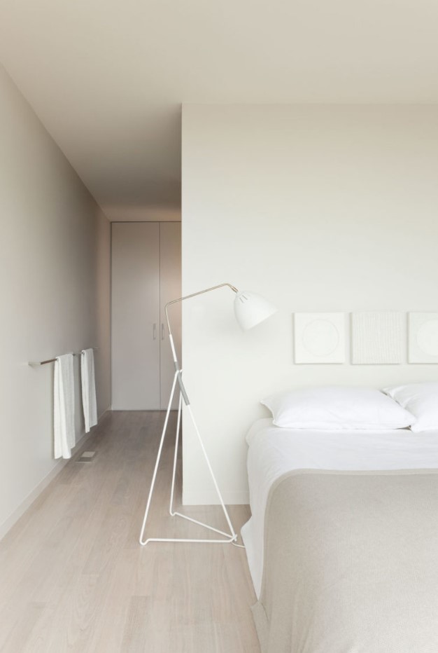 minimalist all white bedroom, with closed and hidden storage, a large bed, floor lamps and neutral textiles