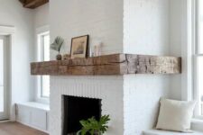 white brick walls and windowsill daybeds, rough wooden beams on the ceiling and a wide rough wood mantel that contrasts the brick