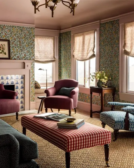 a catchy vintage living room with green floral wallpaper, a green sofa, burgundy chairs and a blue one, a plaid ottoman and a printed rug