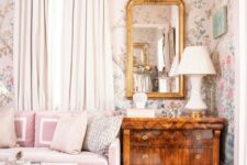 03 a catchy vintage living room with neutral floral wallpaper, a pink sofa with neutral pillows, a stained dresser, a mirror in a gold frame
