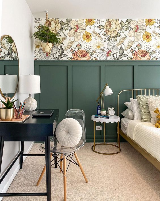 a chic bedroom with green wall paneling and botanical wallpaper, a forged bed and a nightstand, a black vanity and a clear chair