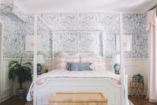 05 a cottage bedroom with blue floral wallpaper, a white bd with printed bedding, a woven chest, potted plants and a chandelier