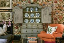 05 a maximalist cottagecore living room with bright floral wallpaper, a dark sofa and an orange chair, a black coffee table, a shabby chic buffet