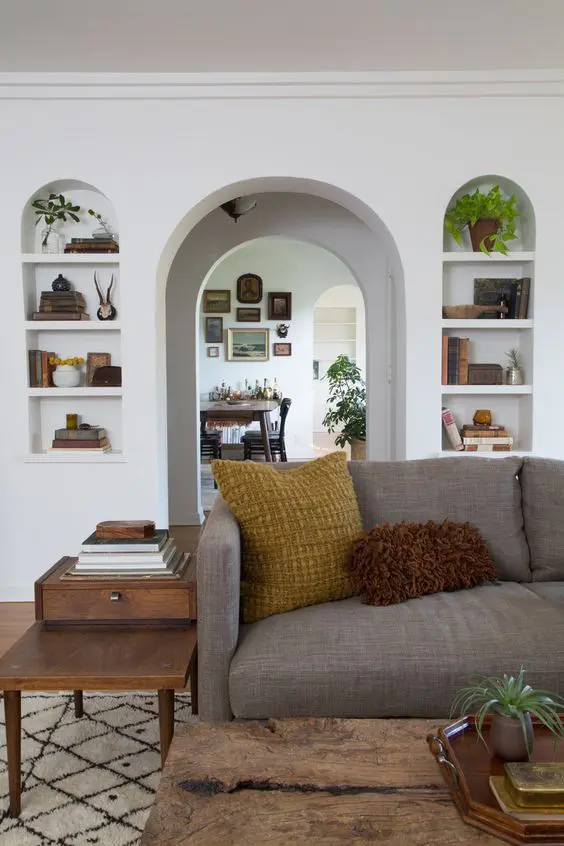 a farmhouse living room with arched niches for decor and an arched doorway, with a grey sofa and stained tables plus potted plants