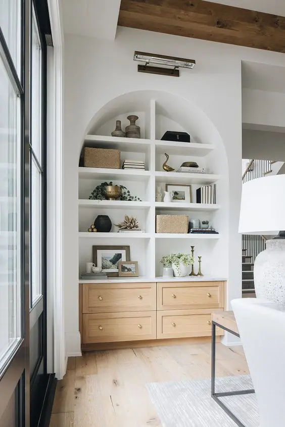a large arched niche with built-in shelves and storage units, with books, decor and artwork is a stylish addition to living room decor