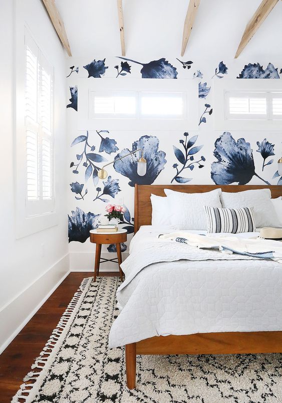 a lovely bedroom with a bold blue floral accent wall, a stained bed and nightstands, neutral bedding and a printed rug