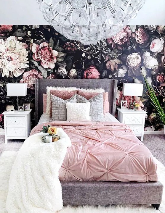 a realistic floral wallpaper wall, a grey bed with pink bedding, white inlay nightstands and a chic crystal flower chandelier