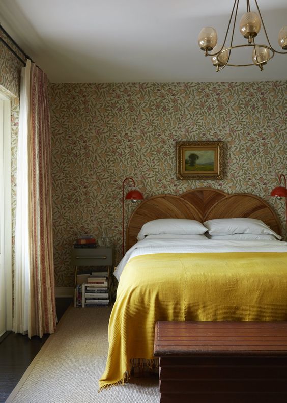 a vintage bedroom with floral wallpaper, a bed with a wooden headboard, neutral and yellow bedding, nightstands and red lamps