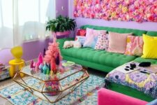 18 a super colorful maximalist living room with a bright faux flower wall, a green sofa, a hot pink chair, colorful pillows, a diamond-shaped glass table