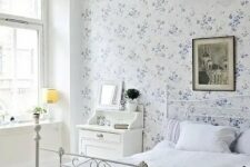 18 a vintage-inspired bedroom with a blue floral wall, a white forged bed, white furniture, a dark artwork and a pendant lamp