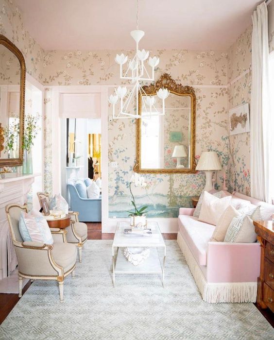 an English living room with floral wallpaper, a non-working fireplace, grey chairs, a pink sofa, a coffee table and large mirrors