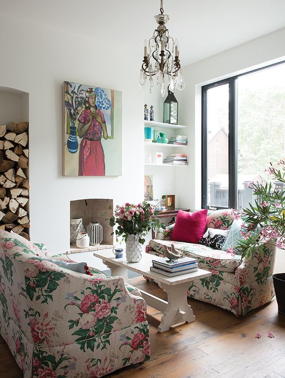 a chic living room with a non-working fireplace, floral sofas, a bench as a coffee table, a crystal chandelier