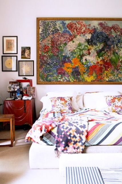 a neutral bedroom with a white bed and colorful bedding, a stained nightstand and a gallery wall including a huge floral artwork