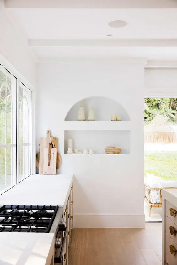 an airy white kitchen with an arched niche with beautiful tableware on display is a chic and lovely space