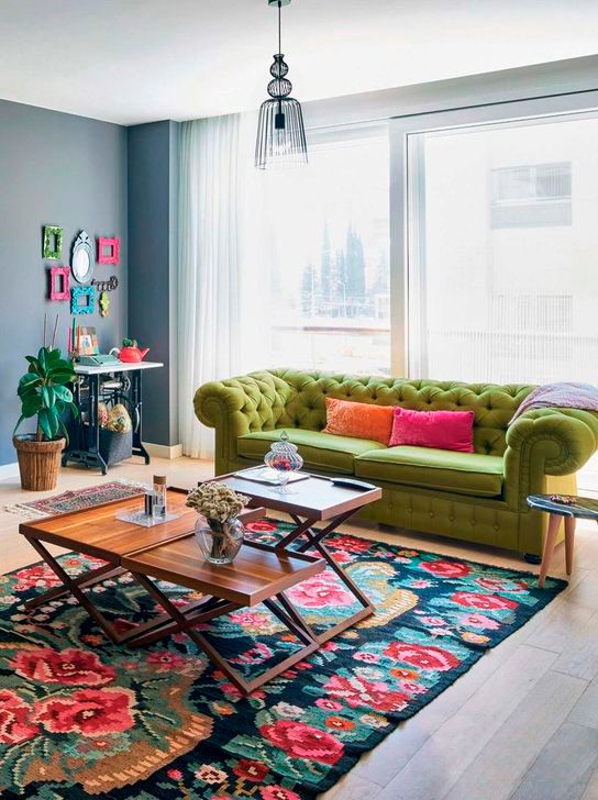 a colorful living room with a bold floral rug, a grene sofa, coffee tables, a console table and a bright gallery wall of frames