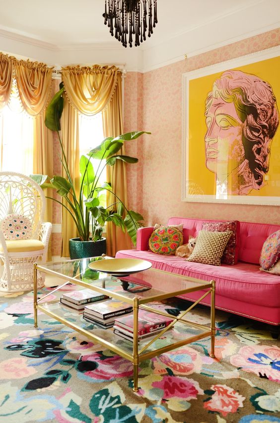 a colorful living room with pink floral wallpaper, a hot pink sofa, a papasan chair, a glass coffee table and a bold floral rug