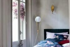 34 a chic bedroom with concrete walls, a black bed with pink, navy and black floral bedding, chic gilded lamps and a stack of books