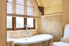 37 a cozy and refined warm-colored bathroom clad with tiles, with an arched niche with a metal clad bathtub and a vintage chandelier