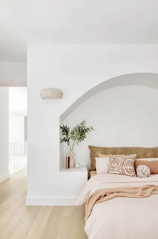a large arched niche that features built-in nightstands and a bed with neutral and pastel bedding right inside