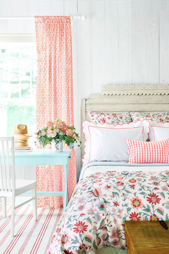 an airy cottage bedroom with slatted walls, a shabbychic bed with bright floral bedding, a mint blue vanity and bold coral curtains