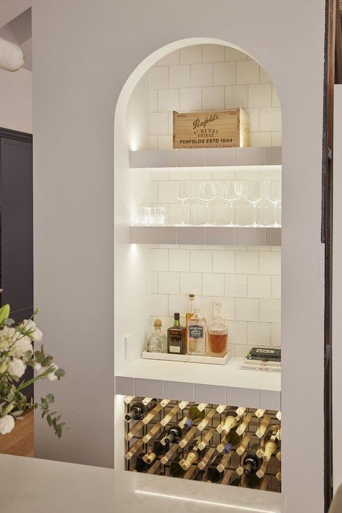 an arched niche clad with square tiles, with built-in lights is used for storing wine bootles, like part of a home bar