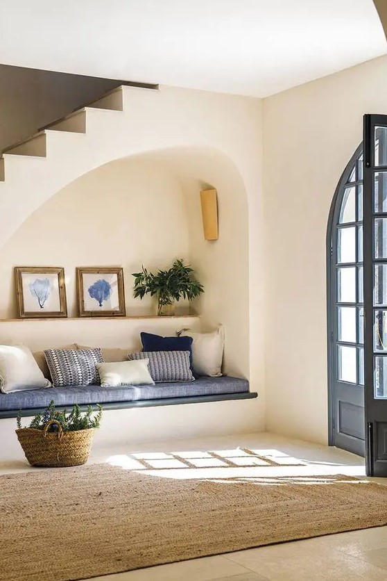 an arched niche with a built-in sofa with pillows, a shelf with art and greenery plus a lamp is a cool solution for an entryway