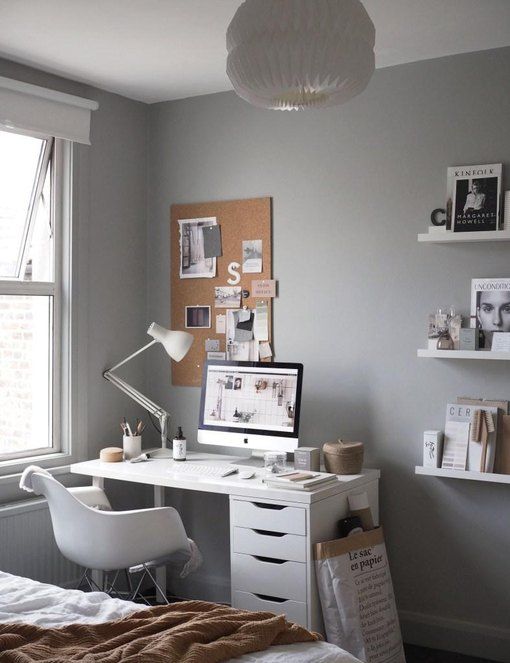 a Scandinavian bedroom with grey walls, a bed with neutral bedding, a white IKEA desk, a white chair, open shelves