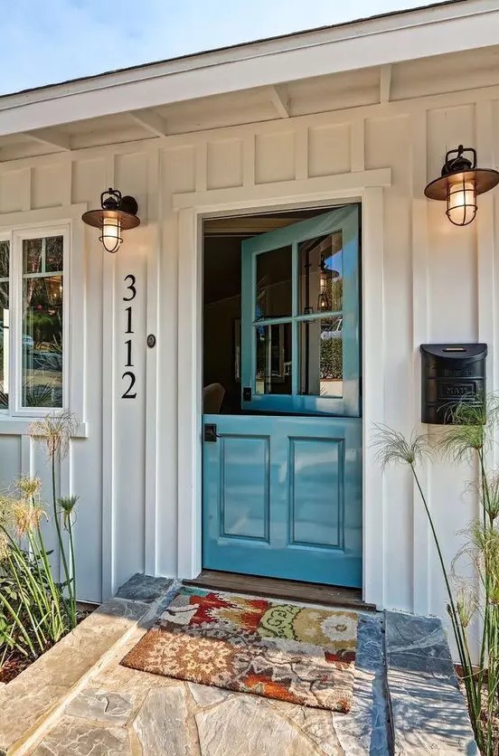 a beach cottage entrance with a beautiful blue Dutch door and cute vintage wall sconces plus greenery on both sides of the door