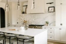 a beautiful modern kitchen with white shaker cabinets, a white quartz backsplash, a white kitchen island and glass pendant lamps