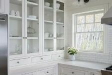 a beautiful white kitchen with inlay and glass cabinets, stainless steel handles and knots, a white subway tile backsplash