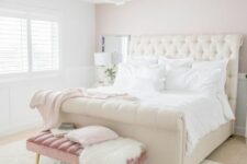 a bedroom with a pale pink accent wall, a creamy upholstered bed, a dusty pink upholstered bench and a grey chair
