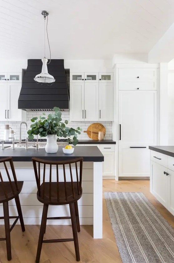 a black and white farmhouse kitchen with white shaker cabinets, black countertops, white tiles on the backsplash and stained stools