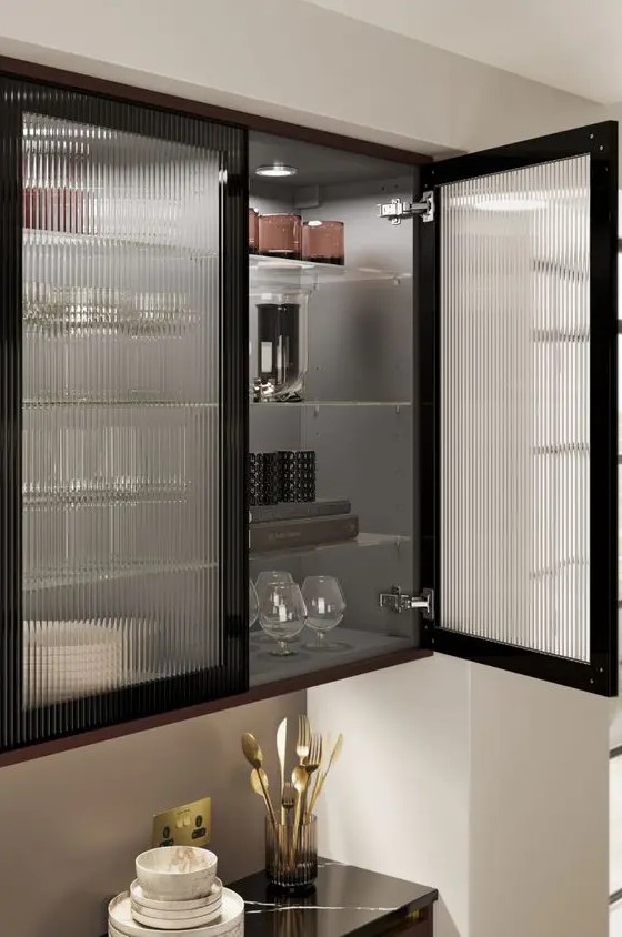 a black kitchen with fluted glass cabinets and lights inside that are great to display dishes and glasses is a chic idea
