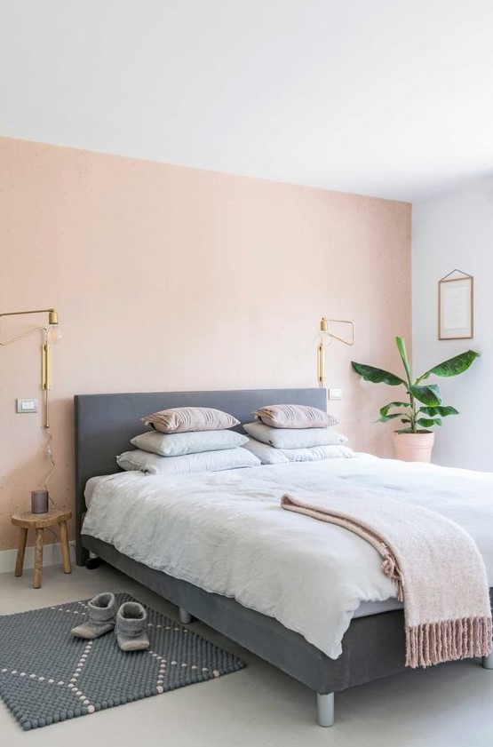 a boho chic bedroom with a light pink accent wall, an upholstered bed, pastel bedding and a printed rug