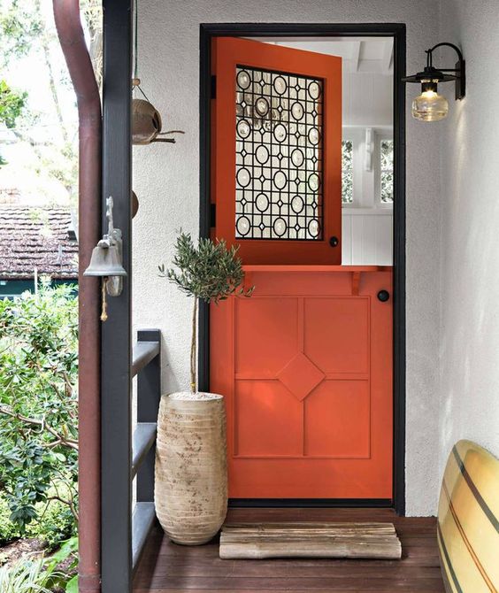 a bright porch with an orange and black Dutch door, a potted plant, a sconce and a bell plus a wooden rug