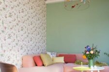 a candy-colored living room with a floral accent and green wall, a low pink sofa with bright pillows, a coral chair and a couple of coffee tables