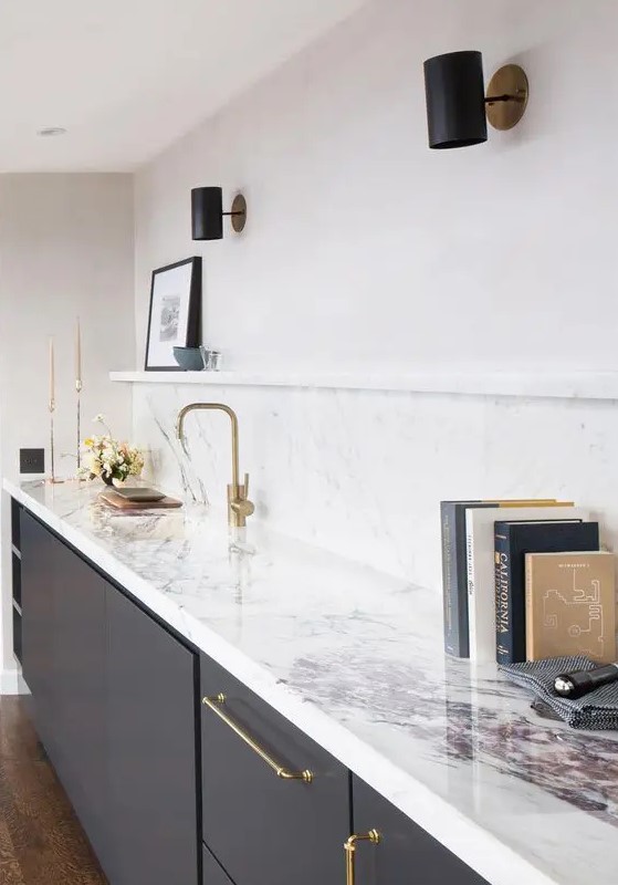 a charcoal grey kitchen with a white quartz backsplash and countertops plus gold fixtures and black spotlights