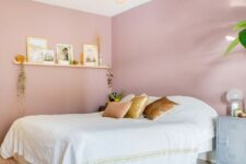 a chic and girlish bedroom with pink walls, a white bed, a floating shelf and touches of gold for more chic