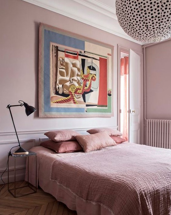 a chic bedroom with light pink walls, pink bedding and a statement artwork and a polka dot lamp