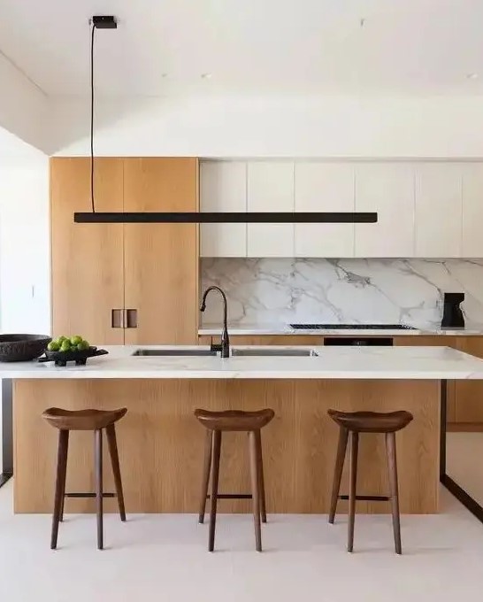 a chic contemporary kitchen with white and light stained cabinets, a large kitchen island with a white stone countertop and a backsplash, a black pendant lamp