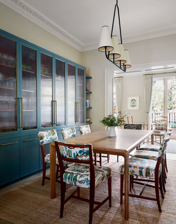 a chic dining room with blue fluted glass cabinets, a stained table and bright upholstery chairs plus a chic chandelier