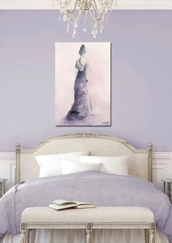 a chic feminine bedroom in lilac and neutrals, with lilac walls, neutral refined furniture, lilac bedding and an artwork plus a crystal chandelier