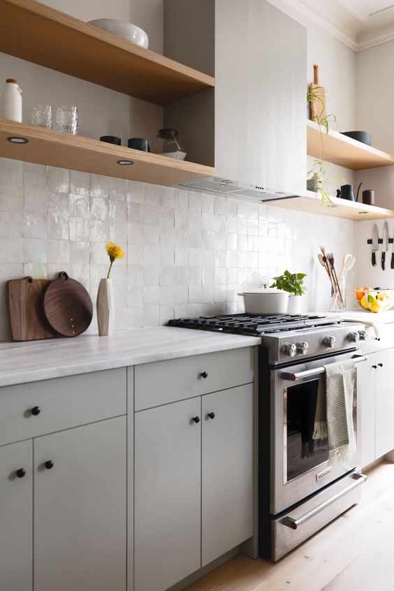 a chic light grey flat panel kitchen with white Zellige tiles and white stone countertops plus open shelves is a cool and cozy space