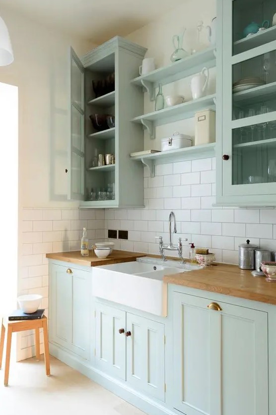 a chic mint green farmhouse kitchen with shaker style cabinets, butcherblock countertops, a white subway tile backsplash and a vintage faucet