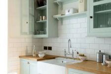 a chic mint green farmhouse kitchen with shaker style cabinets, butcherblock countertops, a white subway tile backsplash and a vintage faucet